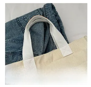 Detail showing white corduroy tote bag texture with large front pockets and woven handles