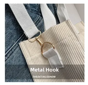 Detail of off-white corduroy tote bag featuring a sturdy golden metal hook and white strap