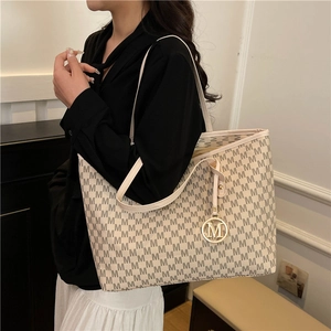 Large beige tote bag with black letter print and gold pendant shown on model