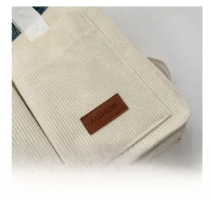 Close-up of beige corduroy fabric texture with brown leather fashion label on tote bag