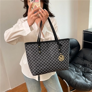 Large capacity tote bag with M-letter pattern held by model in casual indoor setting