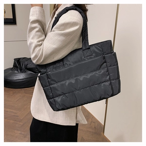 Side view of black quilted nylon tote bag worn by a model in a minimalist setting