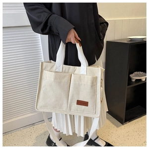 Close-up of cream corduroy tote bag featuring two front pockets and brown leather patch