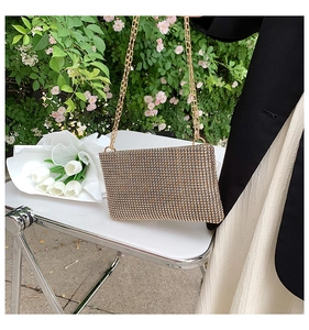 Champagne gold rhinestone clutch bag with gold chain strap shown in a lush garden setting