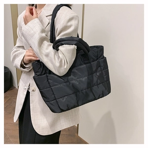 Close-up of black quilted nylon tote bag with thick handles and side pocket on a model