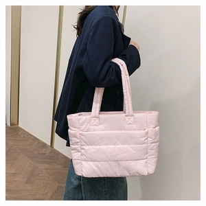 Model wearing a pink quilted nylon tote bag with wide shoulder straps in a bright room