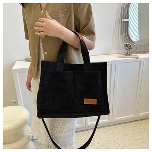 Detail of black corduroy tote bag showing front pockets and brown leather brand label