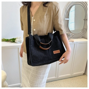 Detailed view of black corduroy tote bag with brown leather handles and FASHION patch