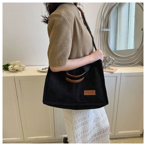 Detail of black corduroy tote bag with brown leather handles and fashion logo patch