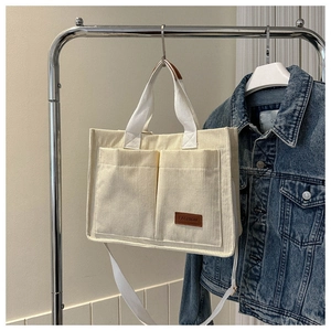 Detail of off-white corduroy tote bag showing front pockets and fashion leather label