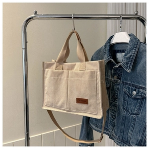 Detailed view of beige corduroy tote bag with double front pockets and brown logo patch