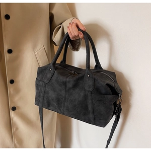 Detail view of a charcoal gray frosted leather Boston bag held by a model in a trench coat
