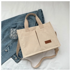 Close-up of beige corduroy tote bag showing large front pockets and FASHION leather tag