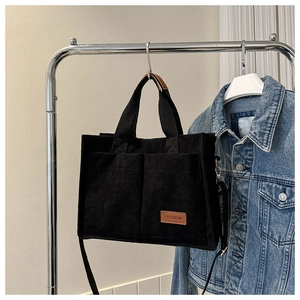 Detail view of black corduroy tote bag featuring dual front pockets and adjustable strap