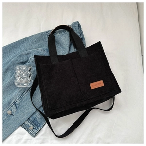 Detailed macro view of black corduroy tote bag with brown leather FASHION label and texture