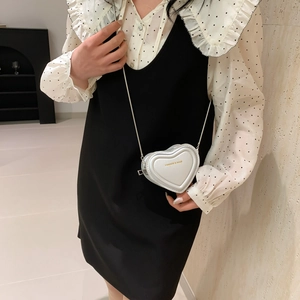 Mini sac à bandoulière argenté en forme de cœur avec chaîne en métal porté par un mannequin
