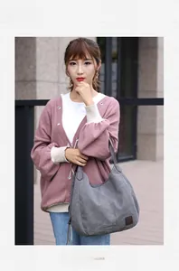 Detail shot of grey canvas tote bag with brown leather straps in a casual outdoor setting