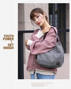Gray canvas tote bag featuring leather handles and embossed logo on casual model outfit