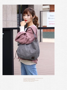 Detail of grey canvas tote bag with brown leather straps shown in a lifestyle street setting