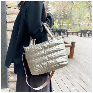 Gewatteerde champagne puffer tote tas gedragen als crossbody door een model in een park