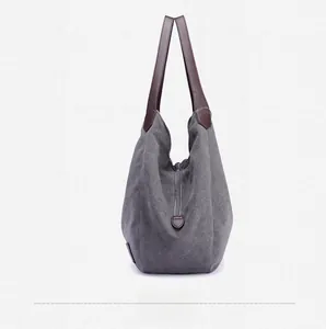 Side view of gray canvas tote bag with brown leather handles and reinforced stitching