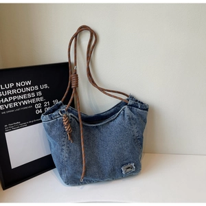 Detail of blue denim tote bag with woven rope shoulder straps and metal buckle accent