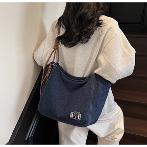 Detail of blue denim tote bag featuring woven rope straps and cow print patch decoration