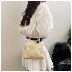 Detail of a beige straw shell bag with gold chain strap and metal clasp on a white dress