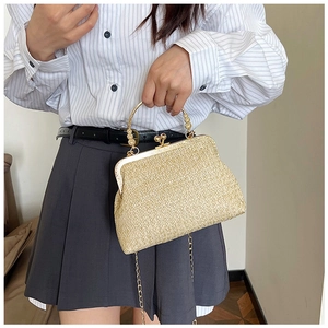 Detail of a beige woven straw shell bag with metal chain strap on a model