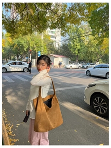 Detail of a large brown suede tote bag with metal buckle on a sunny autumn street