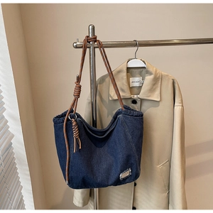Detail of blue denim tote bag with brown rope handles and fringe edges hanging on a rack