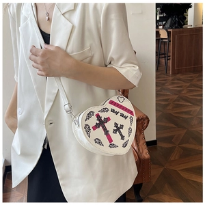 Détail du sac bandoulière crème en forme de cœur avec imprimé croix rose et métal argenté