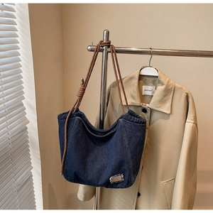 Detail of blue denim tote bag with brown braided rope shoulder straps and metal accent