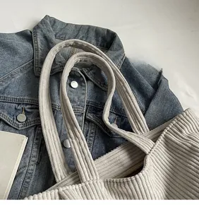 Dettaglio borsa tote beige in velluto a coste con spalline lunghe su denim blu