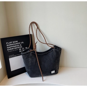 Detail of dark grey washed denim tote with brown braided rope handle and white logo tag
