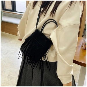 Detail shot of black faux suede tassel handbag with round handle and shoulder strap
