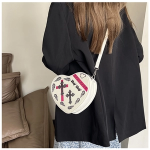 Vue détaillée du sac bandoulière blanc en forme de cœur avec imprimé croix et texte baby