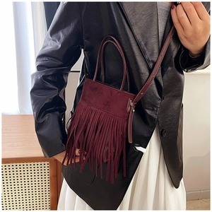 Detail shot of a burgundy suede crossbody bag featuring dense fringe tassels and leather strap