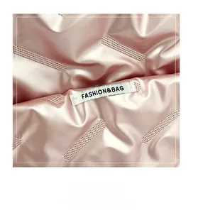 Détail du tissu satiné rose matelassé avec étiquette blanche rectangulaire et texte
