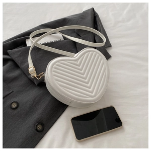 Détail d'un sac bandoulière en forme de cœur avec matelassage en V près d'un mobile