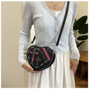 Détail d'un sac bandoulière en forme de cœur avec croix pailletées et rivets cœurs