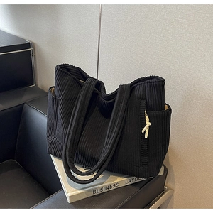 Dettaglio borsa tote in velluto a coste nero con tasca laterale e nappina con nodo bianco