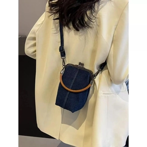 Detail view of deep blue denim crossbody bag with wood handle on white blazer