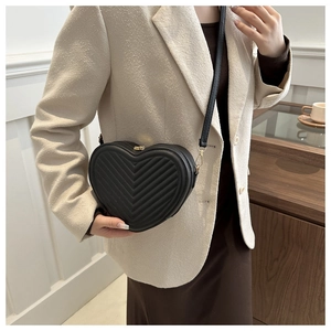 Détail d'un sac bandoulière noir en forme de cœur avec matelassage en V et boucles dorées