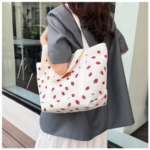 Detail of strawberry print on cream corduroy tote bag with leather logo patch and handle
