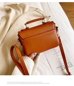 Detail of caramel PU leather handbag with gold hardware on beige knit background