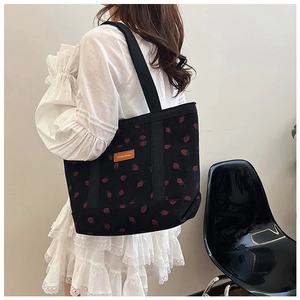 Detail of black corduroy tote bag featuring red strawberry embroidery and yellow leather tag