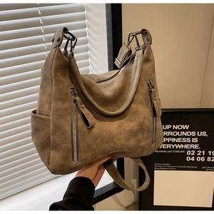 Close-up of brown suede tote bag with metal zippers and adjustable wide shoulder strap