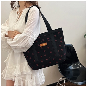 Close-up of corduroy tote bag with red strawberry pattern and brown leather brand label