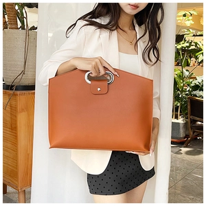 Detail view of large brown PU leather tote bag with unique oval metal handles and snap closure